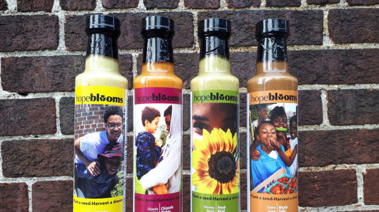 Four bottles of Hope Blooms salad dressing against a brick wall