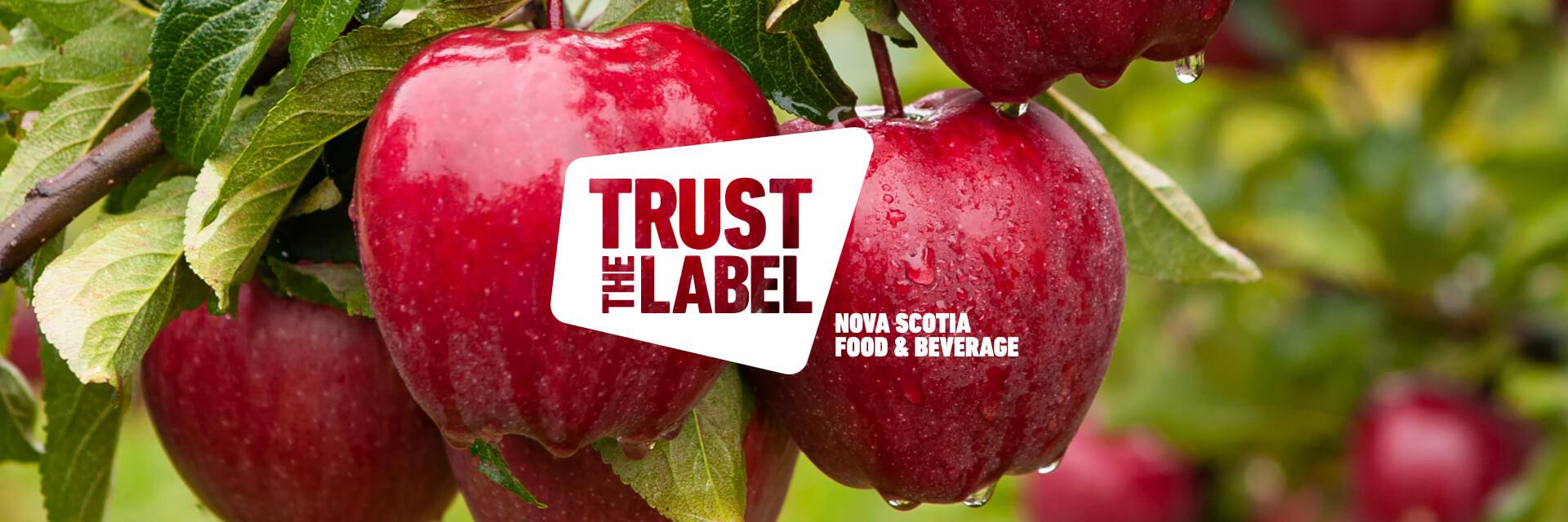 A 'Trust the Label' Nova Scotia Food and Beverage logo overlaid on a photo of red apples on a branch