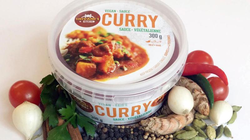 A container of Shivani's Kitchen curry surrounded by ingredients.