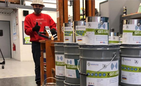 Worker standing behind stacked cans of Graphite Innovation &amp; Technologies product